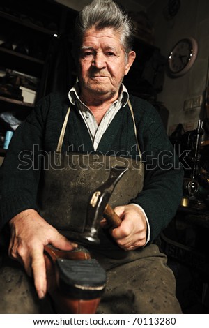 Elderly man in his workshop repairing a shoe with a hammer