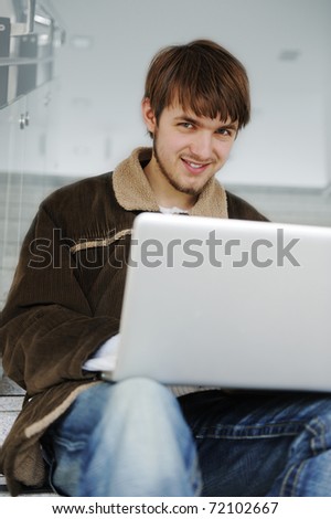 Relaxed young man working on laptop while sitting indoor on  building steps