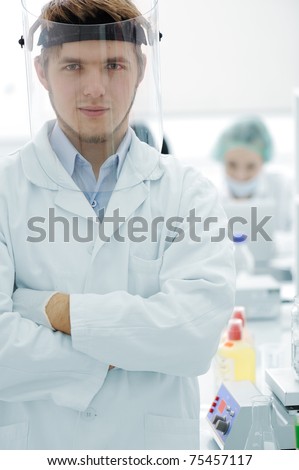 Confident young doctor with mask and folded hands in hospital laboratory