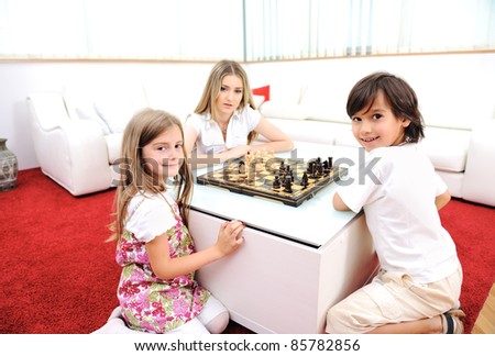 Happy family at home, young mother playing chess with her children