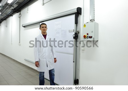 Young worker opening  door of industrial refrigerator