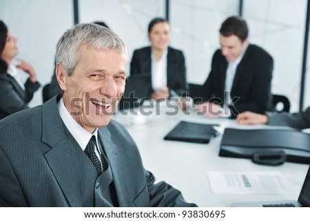Senior businessman at a meeting laughing. Group of colleagues in the background