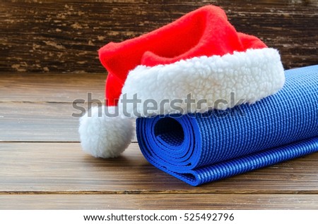 Close up of blue mat with Santa Clause hat on wooden background. Best Christmas gift for active person. Yoga xmas concept.  Copy space