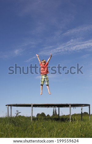 Young boy jumping on a trampoline on green meadow