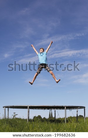 Young boy jumping on a trampoline on green meadow