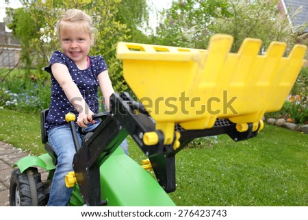Happy young girl plays on a toy tractor outdoors in the garden