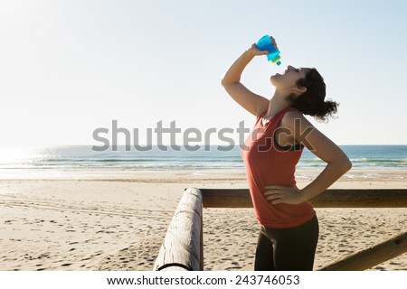 Horizontal photo of a young woman drinking fresh water after sport on the beach.