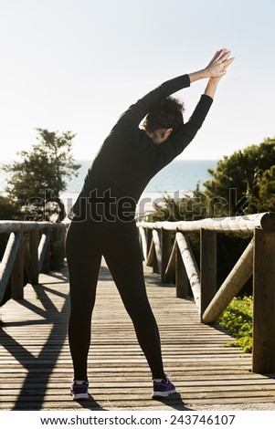 Vertical photo of a young woman stretching her arms at sunset on the path leading to the beach.