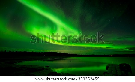 Spinning Lights - Bands of bright northern lights spinning across the starry night sky over a lake.