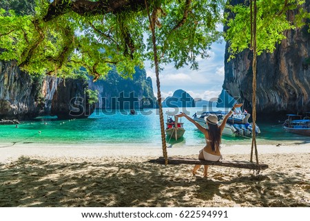 Happy woman in bikini arms open feeling freedom sitting on wooden swing under tree and looking destinations beach, Koh Lao Lading island, Andaman sea, Krabi province, Thailand