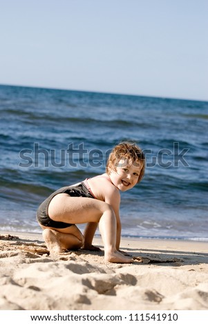 A smiling two year old girl playing in the sand at the beach.