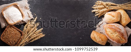 fresh bread with wheat ears and bowl of flour on dark board, top view
