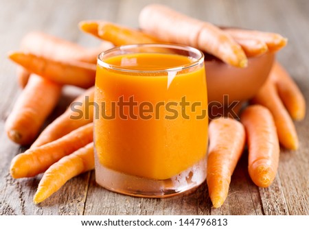 glass of carrot juice with fresh carrots on wooden table