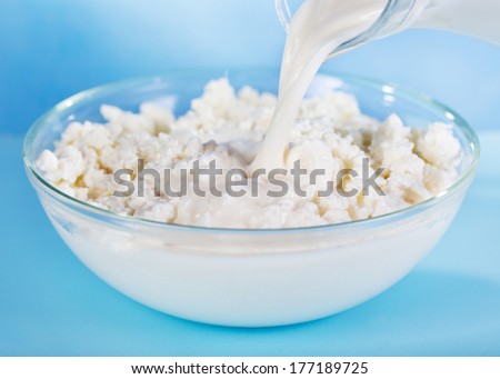 milk pouring into bowl with cottage cheese on blue background