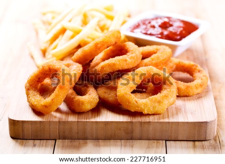 onion rings and fried potato with ketchup on wooden board