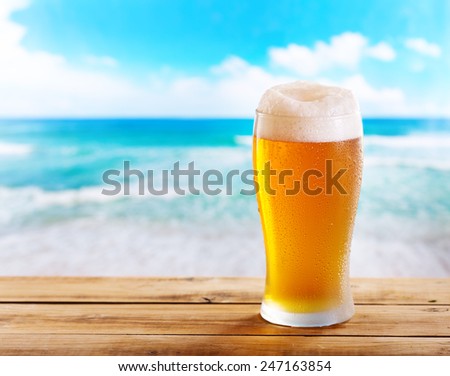 cold glass of beer on wooden table over sea