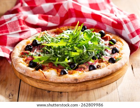 pizza with ham, salami and arugula salad on wooden table