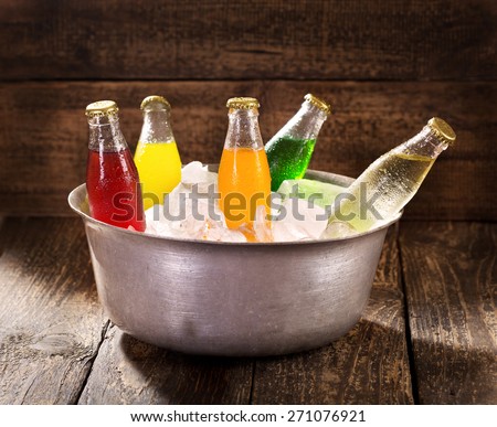 various bottles of soda in the bucket with ice on wooden table