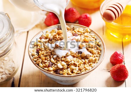 milk pouring into bowl of muesli on wooden table