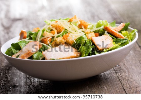 Caesar salad with chicken and greens on wooden table