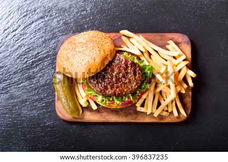 hamburger with vegetables and fries on a wooden board, top view.
