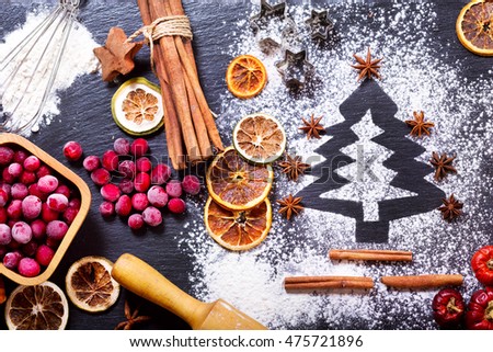 Christmas cooking: fir tree made from flour on a dark table, ingredients for baking, frozen cranberry and dried fruits on dark background, top view