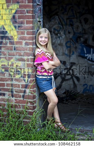 Beautiful little blonde, blue-eyed girl smiling in front of painted graffiti wall