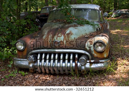 stock photo Junk yard vehicles showing old rusted car in overgrown weedy