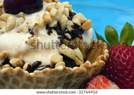 Close up of Vanilla Ice Cream Sundae in an edible waffle bowl with chocolate syrup, nuts, strawberries on the side, and a cherry on top