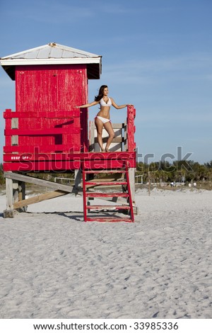 Beautiful smiling young brunette with cute figure wearing  a bikini on lifeguard tower at beach