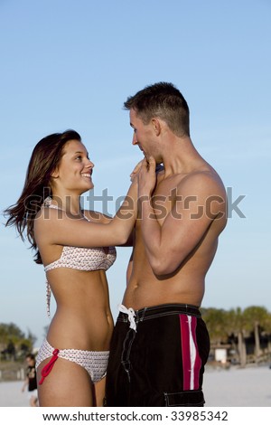 Handsome young man and beautiful bikini clad woman flirting and smiling on beach