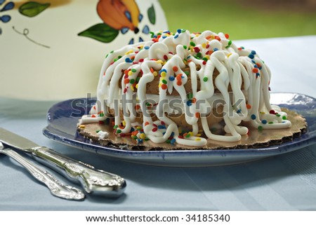 Beautiful decorated cake made from two cookies and frosting, decorated with strings of frosting and sprinkles.  A pitcher of lemonade is in the background, along with natural green outdoor scene.