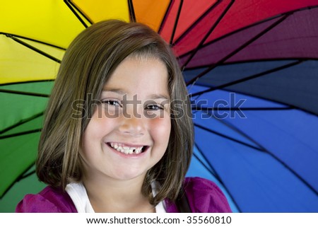 Smiling young brown eyed brunette girl in purple with missing teeth with colorful umbrella