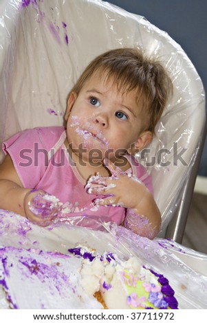 Beautiful messy baby girl eating birthday cake with her hands