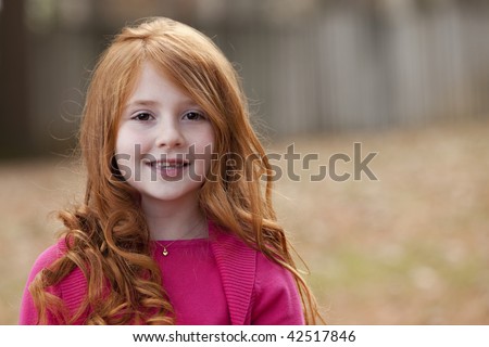 Beautiful smiling little girl with long red hair in pink sweater