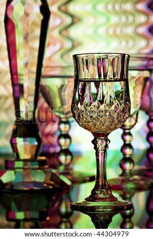 Four Wine glasses and crystal candlestick in front of colorful background with shades of yellow, green, pink and purple.