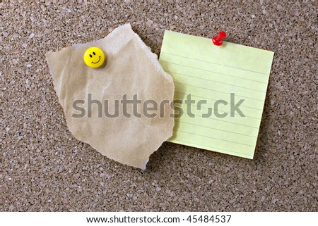 Textured cork bulletin board with a torn scrap of brown paper bag attached with yellow smiling face push pin and yellow note paper attached with red push pin. Ready for your text.