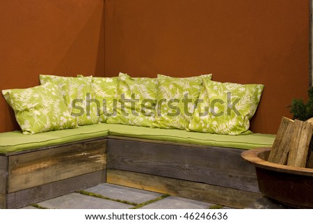 Beautiful green floral patio seating in front of orange stucco wall with firewood bin to the side.