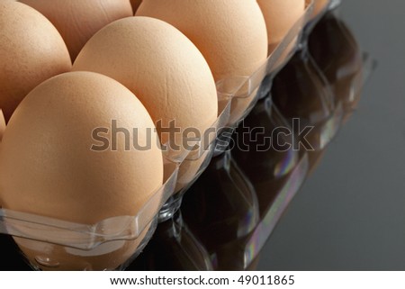 Beautiful brown organic eggs in clear plastic tray reflected on black countertop