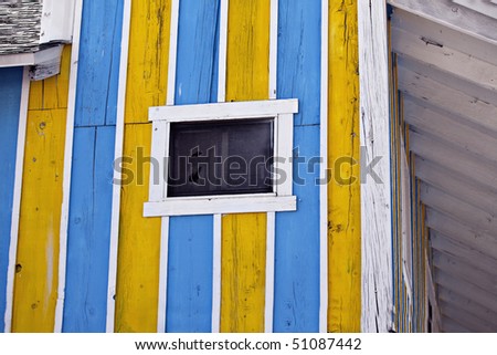 Vibrant yellow, blue and white striped wooden wall with window and torn screen
