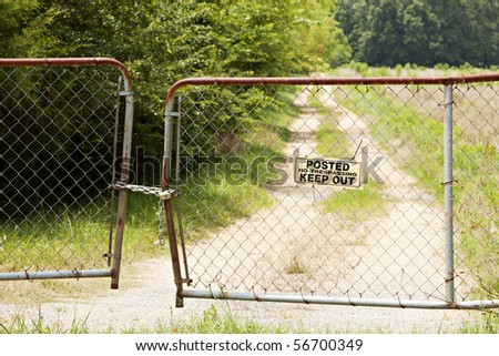 Old bent and rusted fence and gate locked with chain and pad lock with a Posted No Trespassing Keep Out sign