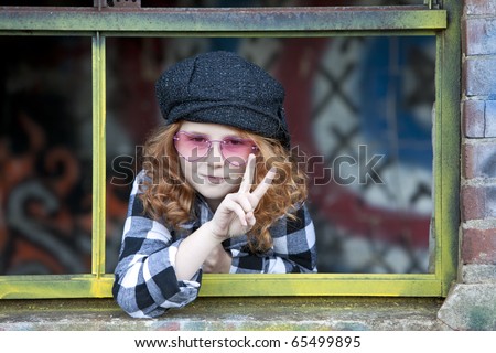 Beautiful young girl with red hair and peace sign  in window of graffiti covered shack