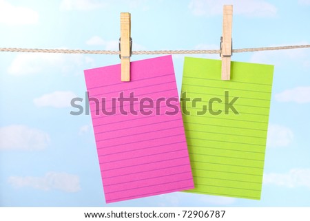 Pink and green paper note cards pinned to clothesline with a blue sky background