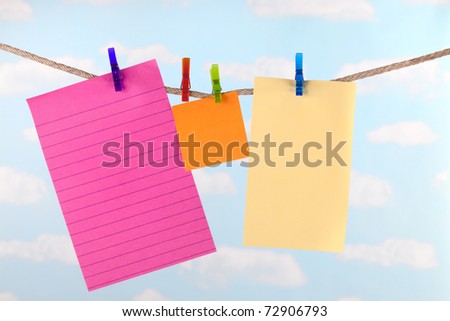 Pink, yellow  and orange paper note cards pinned to clothesline with a blue sky background