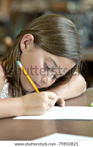 Beautiful  little brunette girl writing with pencil and paper in classroom