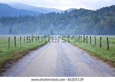 Unpaved country road and pasture lined  with rail fence