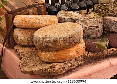 ripe sheep\'s milk cheese on a piece of cork and bottles of Italian wine in background - traditional artisan food product  from Sardinia, Italy