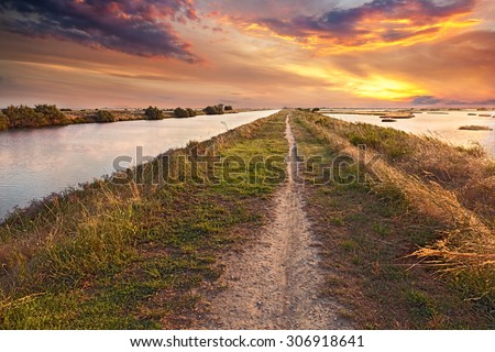 panorama at sunset of the wetland, a long straight path across the lagoon in the natural reserve Valli di Comacchio, near Ferrara, Emilia Romagna, Italy