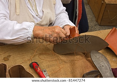 elderly shoemaker in antique costume making medieval shoes ...