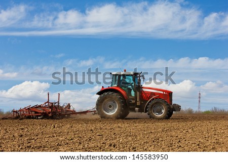 Farmer plowing the field. Cultivating tractor in the field. Red farm tractor with a plow in a farm field. Tractor and Plow
